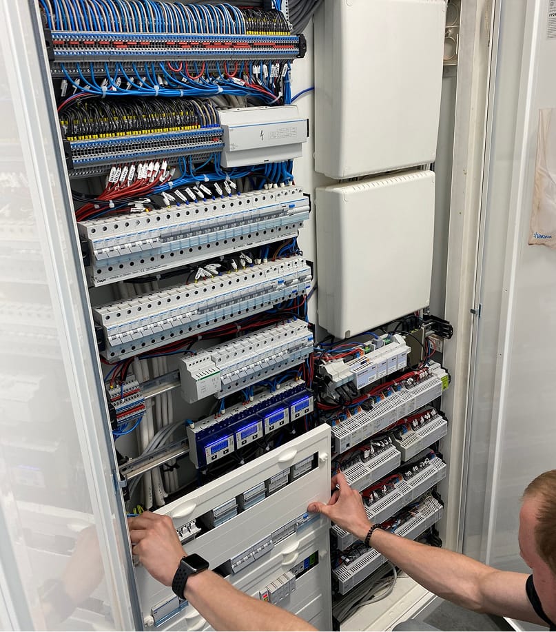 DOMIQ-zostań instalatorzem. Rozdzielnica elektryczna z okablowaniem i osobą serwisującą.